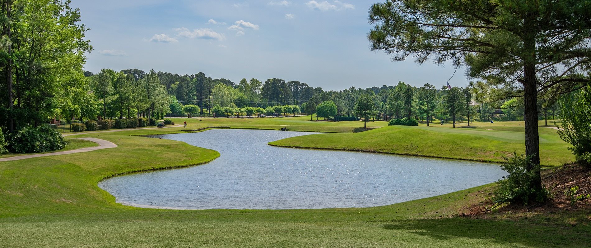 A golf course with a pond and trees in the background.